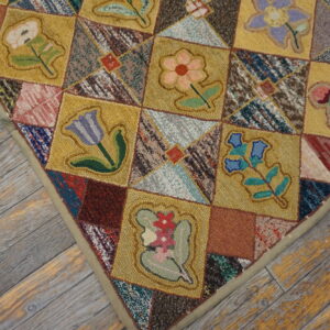 Textured patchwork rug with gold floral squares and multi-colored patches rests on distressed gray wood planks.