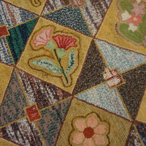 Nubby, multi-colored rug detail shows a yellow and brown patchwork grid filled with various floral designs.