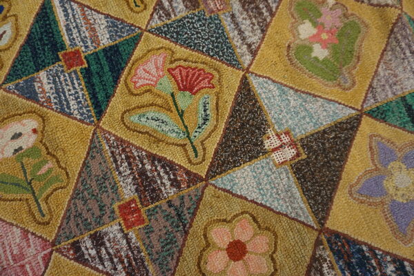 Nubby, multi-colored rug detail shows a yellow and brown patchwork grid filled with various floral designs.