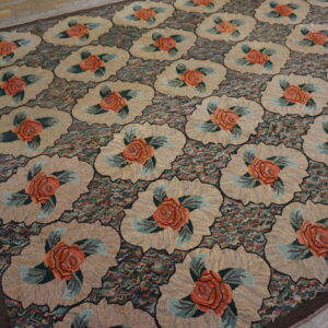 Textured floral rug featuring coral roses in tan medallions set against a multicolored mottled ground on wooden planks.