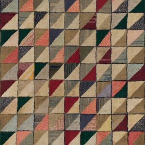 A multi-colored rug with a geometric pattern of triangles rests on weathered wood plank flooring.