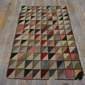 Multicolored hooked rug with a geometric patchwork triangle pattern on weathered plank wood floor.