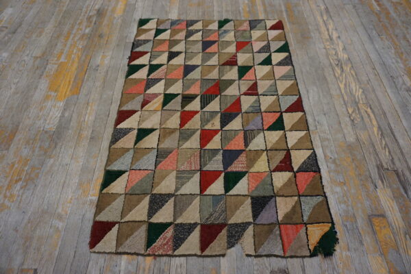 Multicolored hooked rug with a geometric patchwork triangle pattern on weathered plank wood floor.
