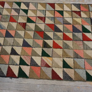 Textured rug with a multicolored patchwork pattern of triangles in red, green, and neutral tones on wood floor.
