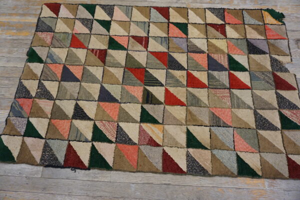 Textured rug with a multicolored patchwork pattern of triangles in red, green, and neutral tones on wood floor.