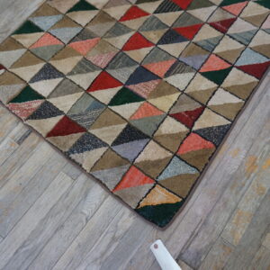 A textured rug with a dense multicolored geometric triangle pattern sits on weathered gray wood.