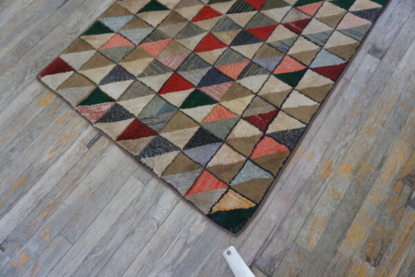 A textured rug with a dense multicolored geometric triangle pattern sits on weathered gray wood.