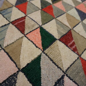 Textured loop pile rug featuring a dense geometric pattern of colorful triangles in red, green, cream, and peach.