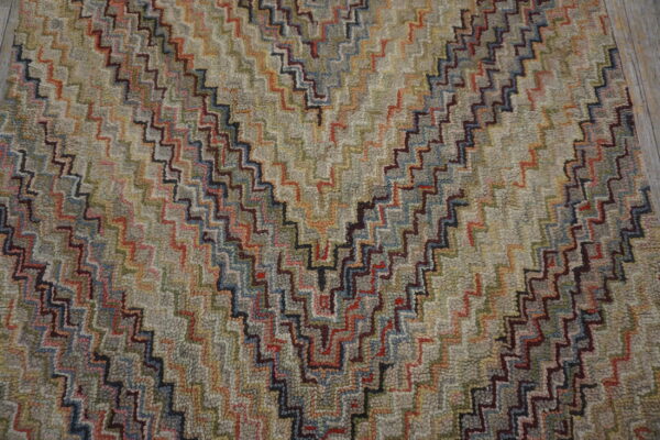 Textured rug with a multicolored stepped zigzag design over a muted gray and beige field.
