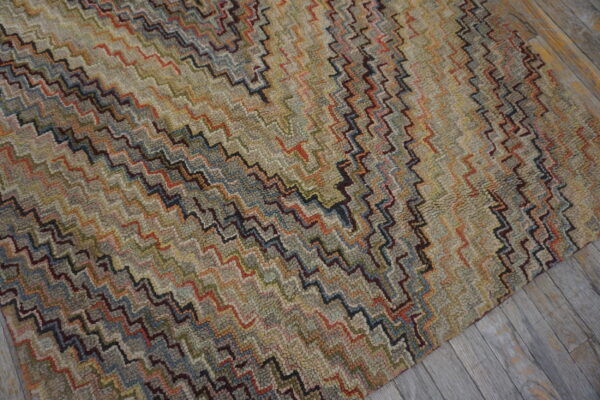 Textured rug featuring dense multicolored zigzag patterns in muted earth tones on grey wooden flooring.
