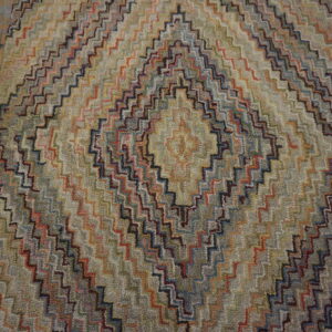 Multicolored, textured rug with a zig-zag diamond pattern resting on weathered gray wood planks.