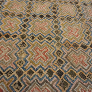 Textured rug surface featuring geometric zigzag and cross motifs in muted blue, pink, gold, and dark green.