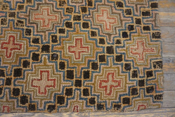 Multicolored textured rug with geometric crosses and dark squares resting on light weathered wood flooring.