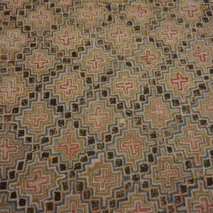 Geometric pattern rug featuring repeating stepped crosses in tan, blue, red, and dark brown accents.