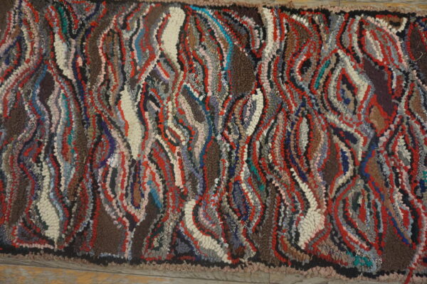 High-pile rug with a textured surface, featuring abstract wavy patterns in red, brown, gray, and cream.