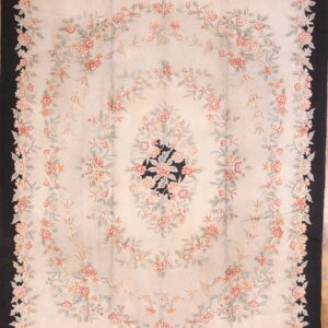 Pale floral rug featuring pink and green garlands, a black border, and a black center medallion on a cream field.