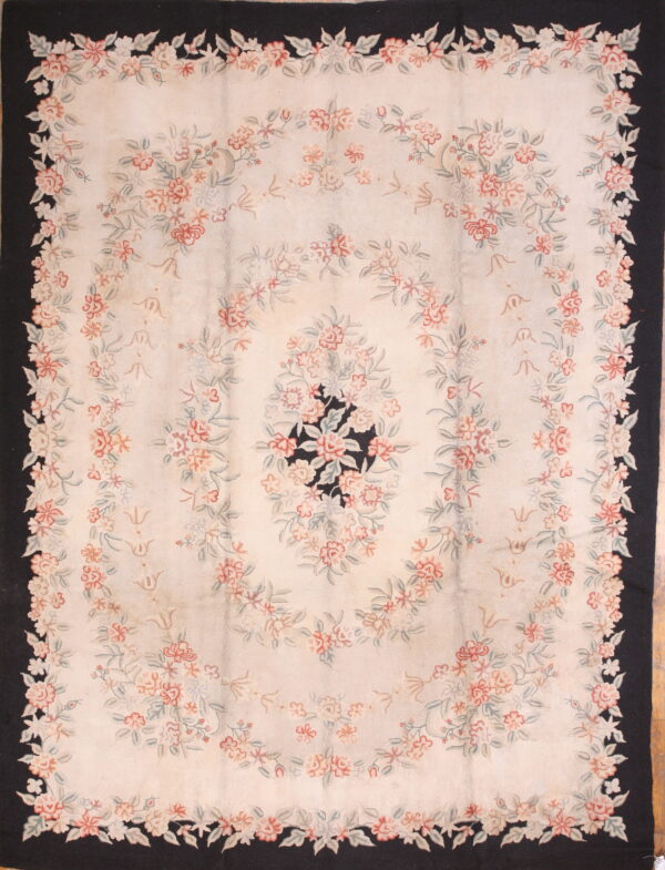 Pale floral rug featuring pink and green garlands, a black border, and a black center medallion on a cream field.