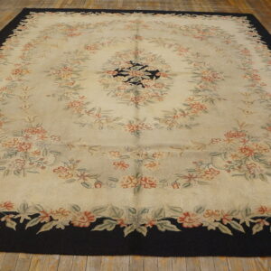 Cream rug with looping coral and sage floral designs and a wide, solid black border on hardwood.