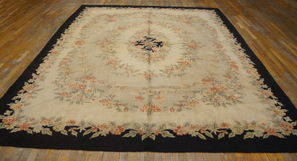 Cream rug with looping coral and sage floral designs and a wide, solid black border on hardwood.