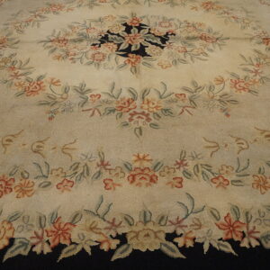 Textured cream rug displaying a dense floral pattern in coral, green, and beige around a visible black ground.