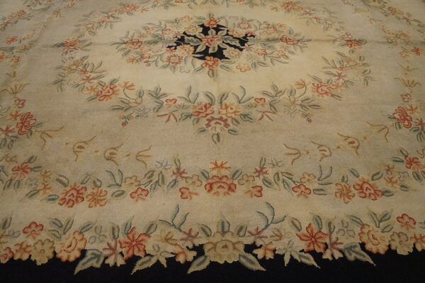Textured cream rug displaying a dense floral pattern in coral, green, and beige around a visible black ground.
