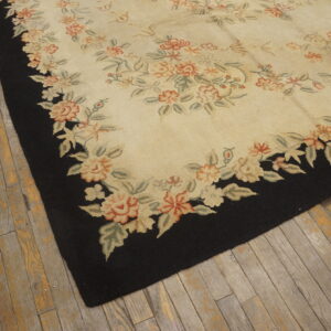 Cream and coral floral rug with a black border sits on distressed wooden flooring.