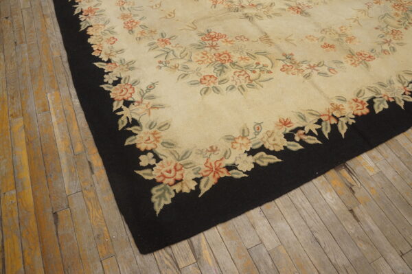 Cream and coral floral rug with a black border sits on distressed wooden flooring.