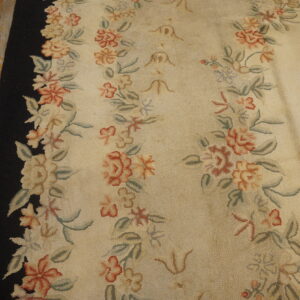 Cream rug featuring textured looped pile, vertical floral rows, and a solid black border on distressed wood.