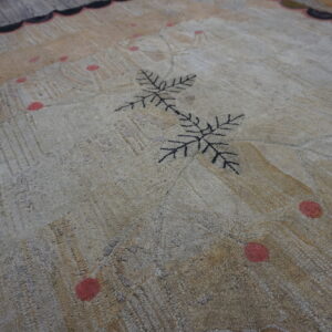 Muted beige textured rug with a black leaf motif and coral spots, lying on gray wooden floorboards.