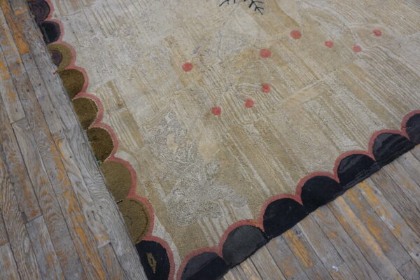Textured beige rug with faint patterns, pink accents, and a scalloped border resting on rustic wood flooring.
