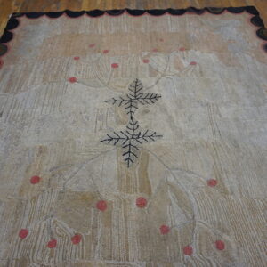 Textured beige rug with a black leafy center, pink dots, and a multicolored scalloped border on wood flooring.