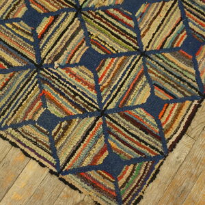 Close-up of a blue and multicolored hooked rug with diagonal fabric strips resting on light wood planks.