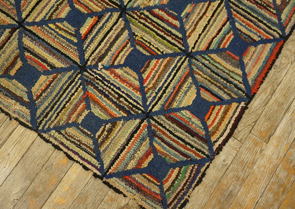 Close-up of a blue and multicolored hooked rug with diagonal fabric strips resting on light wood planks.