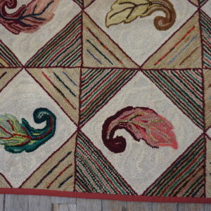 Multicolored looped rug featuring scrolled leaf designs centered in a diamond lattice over light wood flooring.