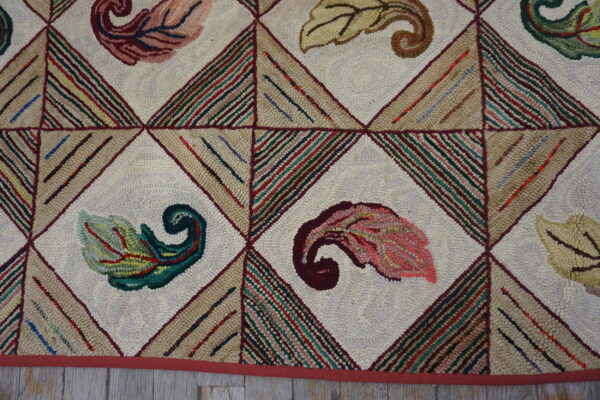 Multicolored looped rug featuring scrolled leaf designs centered in a diamond lattice over light wood flooring.