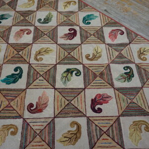 Beige hooked rug with colorful leaves and geometric stripes on gray distressed wood flooring.