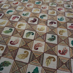 Cream hooked rug with a geometric grid pattern filled with multicolored leaves and textured stripes.