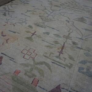Textured cream rug with abstract purple, green, and pink patterns lying on rough concrete flooring.
