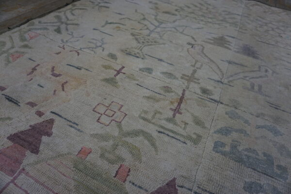 Textured cream rug with abstract purple, green, and pink patterns lying on rough concrete flooring.