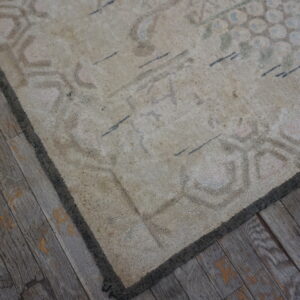 Faded, low-pile beige rug with subtle patterns rests upon rustic, gray plank wood flooring.