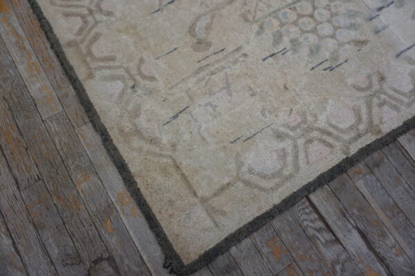 Faded, low-pile beige rug with subtle patterns rests upon rustic, gray plank wood flooring.