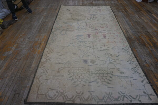 Cream rug with faded abstract patterns in pastel pink, green, and blue, set on rustic wood planks.