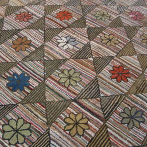 Textured rag rug featuring multicolored floral designs inside striped geometric diamond and triangle patchwork blocks.