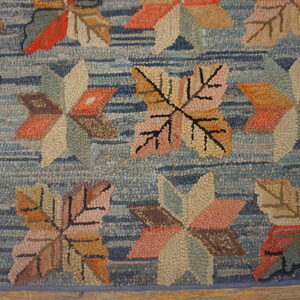Multicolored hooked rug with large leaf patterns on a striped blue background over wood planks.