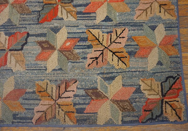 Multicolored hooked rug with large leaf patterns on a striped blue background over wood planks.