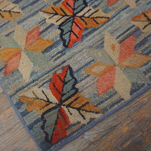 Textured blue rug featuring large stylized orange, red, and beige leaf motifs on rustic wood flooring.