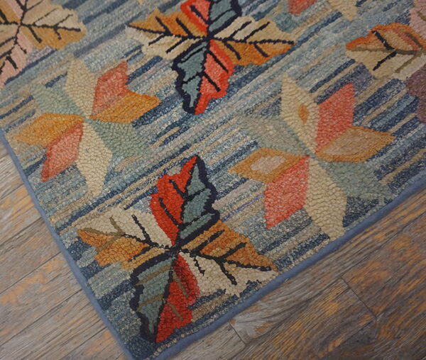 Textured blue rug featuring large stylized orange, red, and beige leaf motifs on rustic wood flooring.