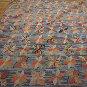 Blue striped rug displays rows of multicolored leaf and geometric star motifs on a textured surface and wood floor.
