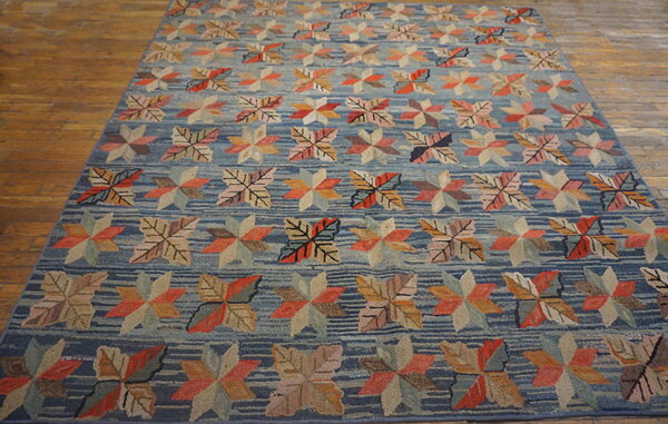 Blue striped rug displays rows of multicolored leaf and geometric star motifs on a textured surface and wood floor.