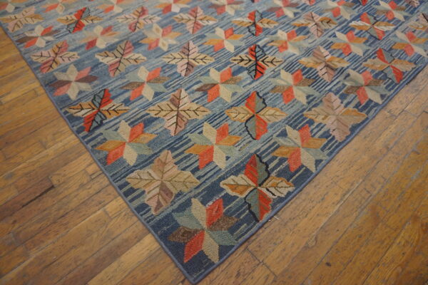 Multicolored floral motifs cover a textured blue rug with diagonal stripes on worn wood flooring.